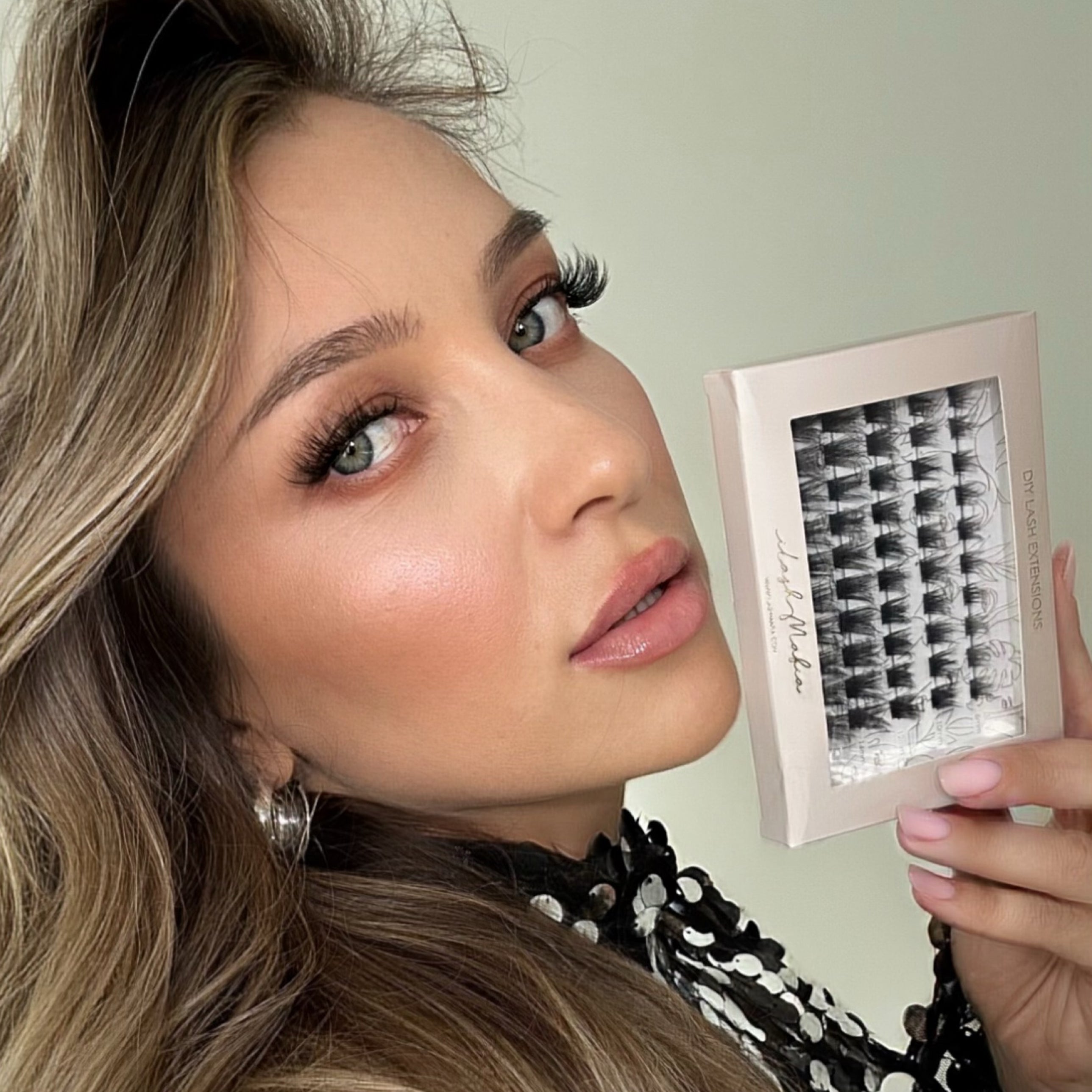 Model wearing iLash Mafia Bestie Vegan DIY lash extensions while holding a tray of reusable lash clusters. The lightweight at-home lash extensions create soft volume, wispy definition, and a natural-looking lash extension effect with customizable doll eye and cat eye styling.