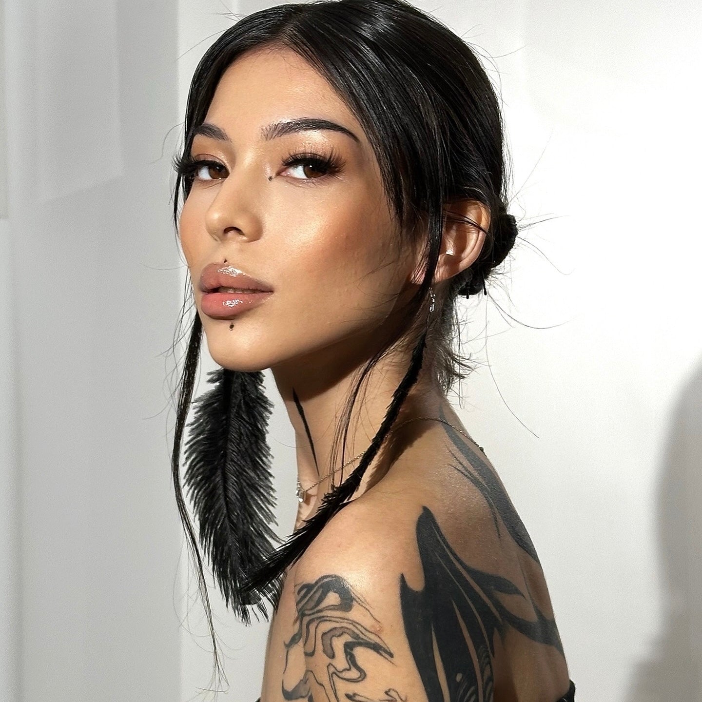 Model wearing iLash Mafia SLAY DIY lash extensions featuring dramatic volume, wispy texture, bold density, and a full-glam effect. Editorial beauty look with dark hair, feather earrings, and artistic tattoos